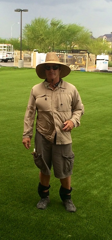 A man in a hat and sunglasses standing on the grass.