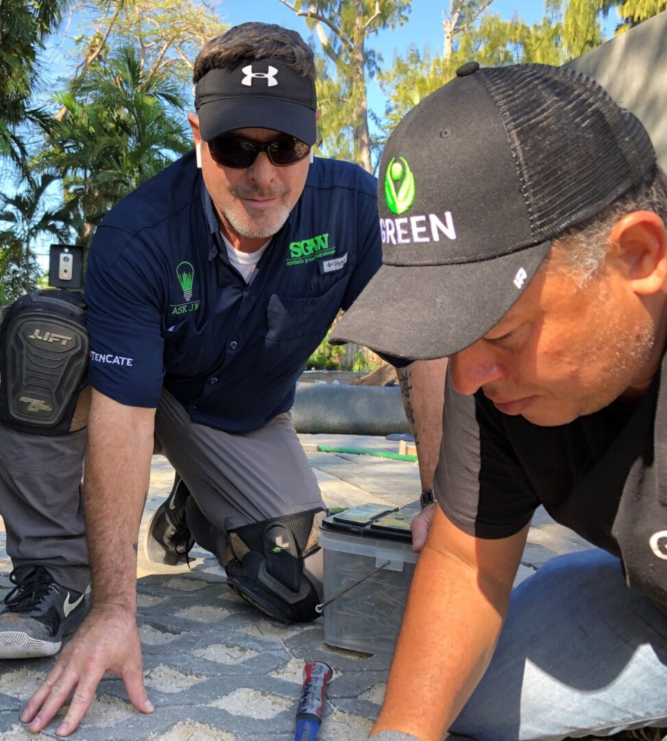 Two men working on a sidewalk with green